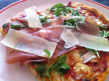 Pizza mit Schwarzwälder-Schinkenspeck, frischem Ruccula, Parmesanscheiben, Zwiebeln und Käse